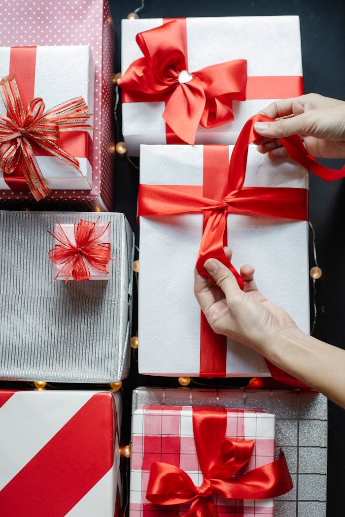 Services Top view of crop unrecognizable person tying red band on present box while preparing for New Year holiday