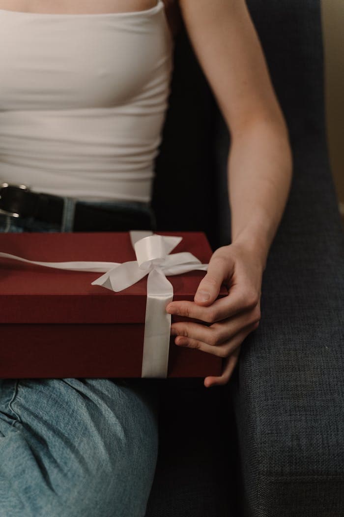 About A person holding a beautifully wrapped gift box with a white ribbon, perfect for special occasions.